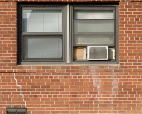 window-ac-unit-outside-red-brick-building-oboys-heating-and-air-removing-and-storing-window-ac-unit-for-winter