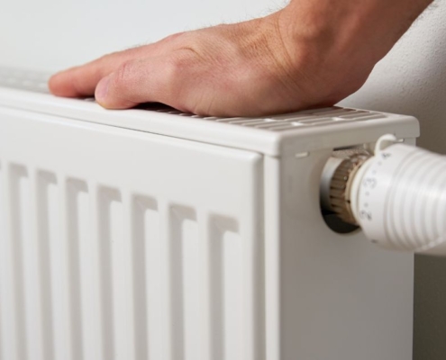 person touching the radiator on their wall - O'Boys Heating & Air radiator